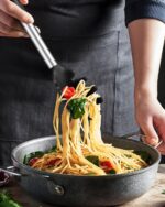 Close-up of a black silicone pasta tong and a polished stainless steel spaghetti spoon with teeth