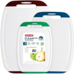 A set of three multicolored Neoflam plastic cutting boards with non-slip handles and juice grooves, stacked on a kitchen coun