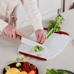 A set of three multicolored Neoflam plastic cutting boards with non-slip handles and juice grooves, stacked on a kitchen coun
