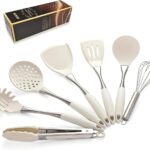 A set of white silicone cooking utensils with stainless steel handles, including a spatula, ladle, spoon, whisk, and tongs.